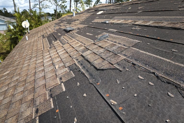 Severely storm-damaged roof with large sections of asphalt shingles blown off and black underlayment fully exposed in Lancaster, PA