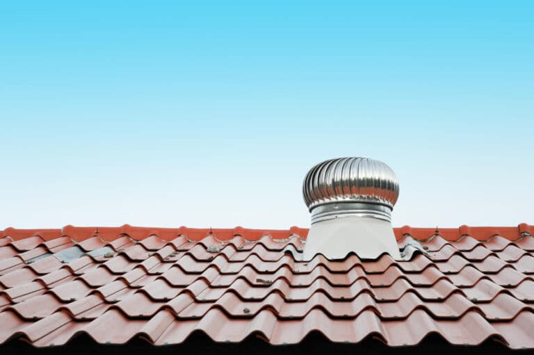 Stainless steel spinning turbine vent installed on a terracotta tile roof against a clear blue sky