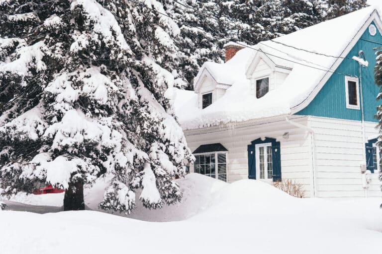Black and white photo of a tiled residential roof buried in deep snow with three small vent caps visible