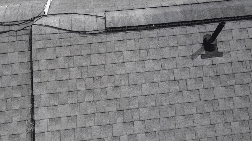 Drone aerial view of a gray asphalt shingle roof showing a ridge vent strip and a black pipe vent