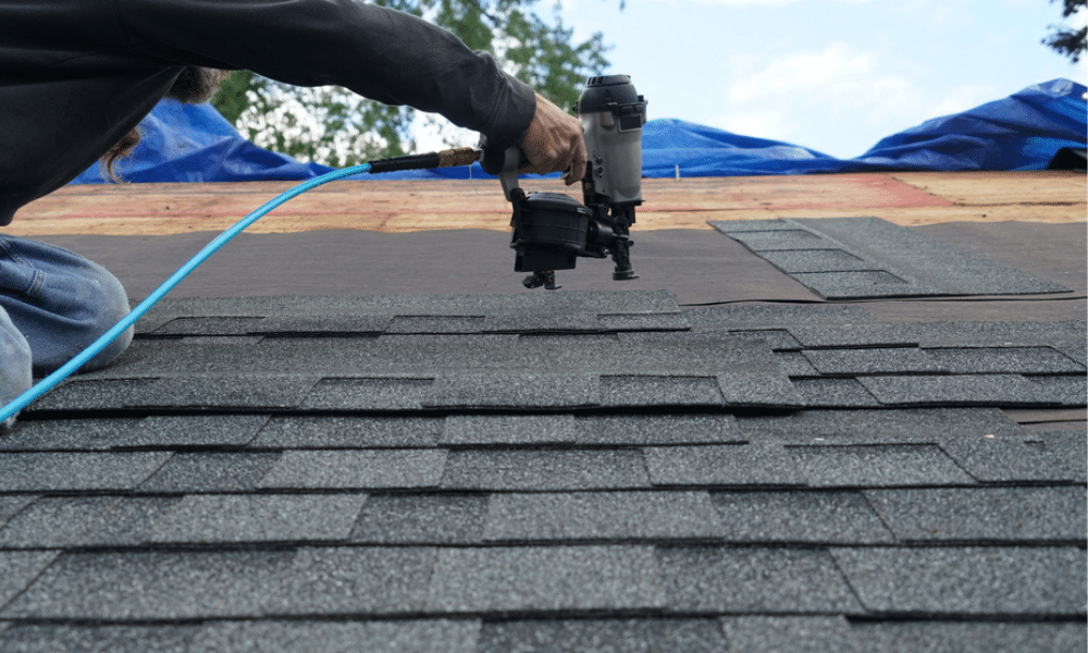 Worker holding a nail gun close to the surface while nailing down charcoal asphalt shingles during a roof repair in Central PA