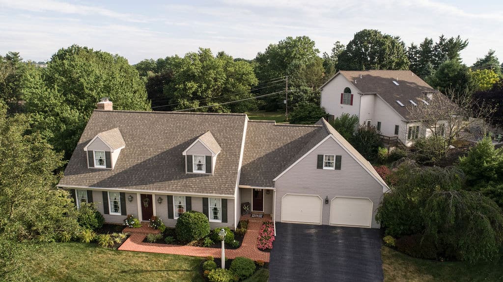 Cape cod style home with gray shingles, dormers, beige vinyl siding, and a neatly landscaped front yard in Lancaster, PA